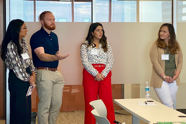 A group of students, three female and one male, standing in a classroom and having a conversation.