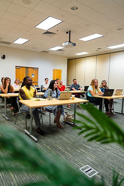 A group of students sits in a lecture hall and listens to instruction.