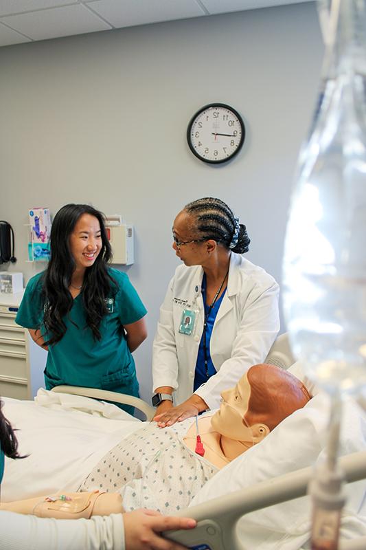 A nursing instructor teaches a nursing student technique on a medical maniken.